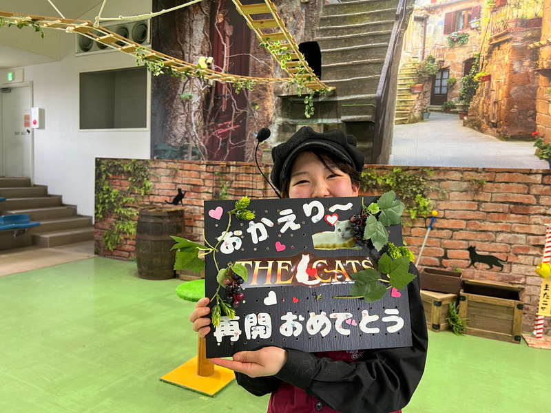 「おかえり〜　THE　CATS　再開おめでとう」と描かれたボードを持って笑顔のショーの担当飼育員橋本さんの写真