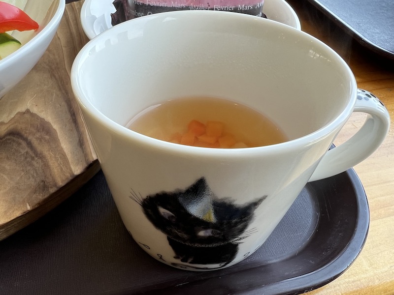 黒猫の絵が描かれたカップに野菜の角切りが入ったコンソメスープ